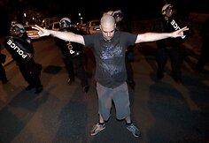 Prie&scaron; policininkus i&scaron;keltomis rankomis stovi protestuotojas
