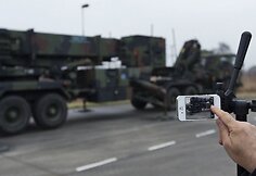 Žurnalistas fotografuoja raketas „Patriot“ vežančią automobilių koloną.
