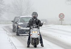 Ant apsnigto kelio stovi vyras su motoroleriu.