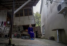 Moteris sėdi &scaron;alia namo, kuris buvo apgadintas per žemės nuo&scaron;liaužą, o &scaron;alia stovinitis naujas namas pradėjo smegti.