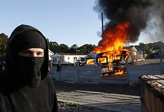 Vaikinas stovi netoli degančio namelio ant ratų