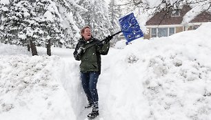 Moteris kasa sniegą šalia savo namų