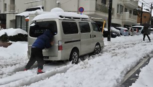 Vyras bando pastumti sniege užklimpusį automobilį.