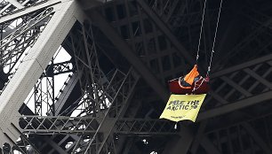 „Greenpeace“ atstovas protestuoja palapinėje, kabančioje ant Eiffelio bokšto sijos.