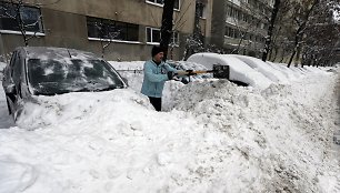 Išvažiuoti besiruošiantis vyras kasa sniegą.