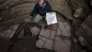 Oferas Sionas, rankoje laikantis Madabos žemėlapio kopiją, stovi ant senojo grindinio.