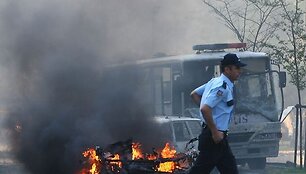 Policininkas bėga pro ma&scaron;inos nuolaužas.