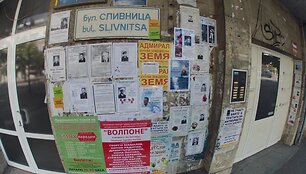 Ant pastato sienų i&scaron;kabinti lapai su čia mirusių žmonių nuotraukomis ir nekrologais