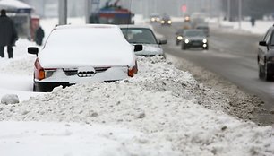 Šalikelėse palikti automobiliai trukdo kelininkams nuvalyti apsnigtas gatves. 