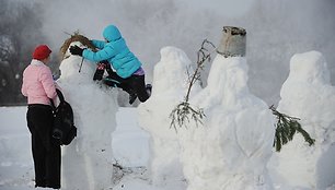 Vaikas deda šieną sniego seniui ant galvos.