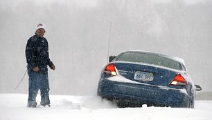 Vyras stovi šalia sniege užklimpusio automobilio.