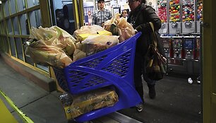 Moteris stumia prekių prikrautą vežimėlį.