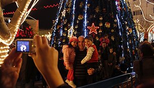 Moteris fotografuoja savo vyrą su vaikais prie Kalėdų eglutės