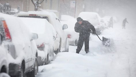 Čikagoje vyras prie savo automobilio kasa sniegą.