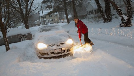 Vyras valo sniegą aplink savo automobilį.