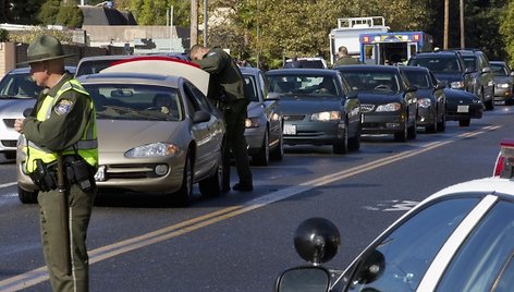 Įtariamojo ieškantys policijos pareigūnai tikrina automobilius.