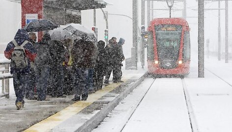 Žmonės, pasislėpę po skėčiais, laukia tramvajaus. 