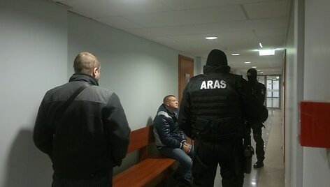 Įtariamasis (sėdi) ir jį saugantys &bdquo;Aro&ldquo; pareigūnai teisme