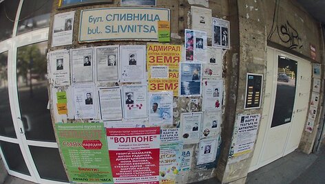 Ant pastato sienų i&scaron;kabinti lapai su čia mirusių žmonių nuotraukomis ir nekrologais