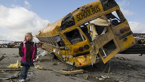 Mergaitė stovi &scaron;alia tornado nuniokoto mokyklinio autobuso