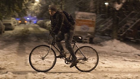 Vyras per sniegą važiuoja dviračiu.