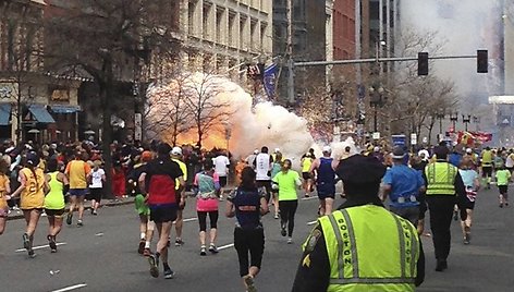 Bostono maratono dalyviai bėga link finišo, kairėje pusėje matomas prasidėjęs sprogimas.