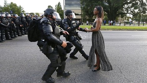 Riaušių policininkai sulaiko neginkluotą proteste dalyvaujančią juodaodę merginą, žengusią link pareigūnų