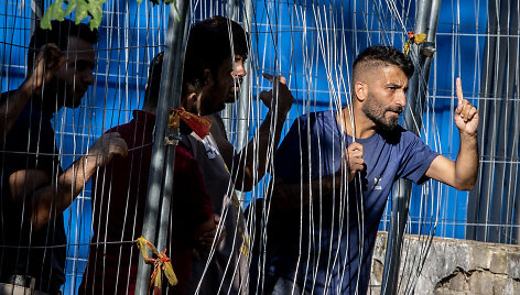 Rūdininkų stovykloje migrantas per i&scaron;ardytą tvorą rodo gestus pareigūnams 