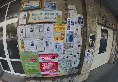 Ant pastato sienų iškabinti lapai su čia mirusių žmonių nuotraukomis ir nekrologais