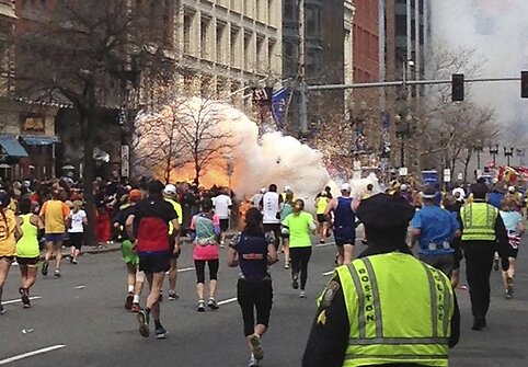 Bostono maratono dalyviai bėga link fini&scaron;o, kairėje pusėje matomas prasidėjęs sprogimas.