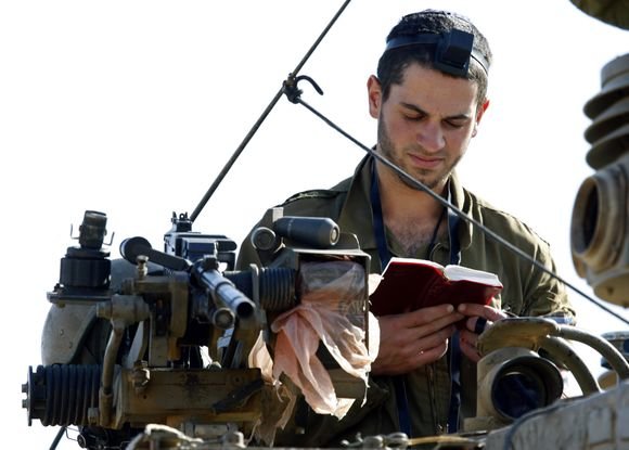 „Reuters“/„Scanpix“ nuotr./Izraelio karys išlipęs iš tanko skaito maldaknygę.