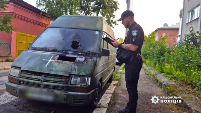 AFP/„Scanpix“ nuotr./Ukrainos policijos pareigūnas apžiūrinėja per padegimą apgadintą automobilį.