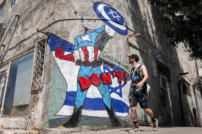 AFP/„Scanpix“ nuotr./Tel Avive vyras eina pro grafitį, vaizduojantį Joe Bideną, apsirengusį kaip „Marvel“ komiksų personažą Kapitoną Ameriką su skydu