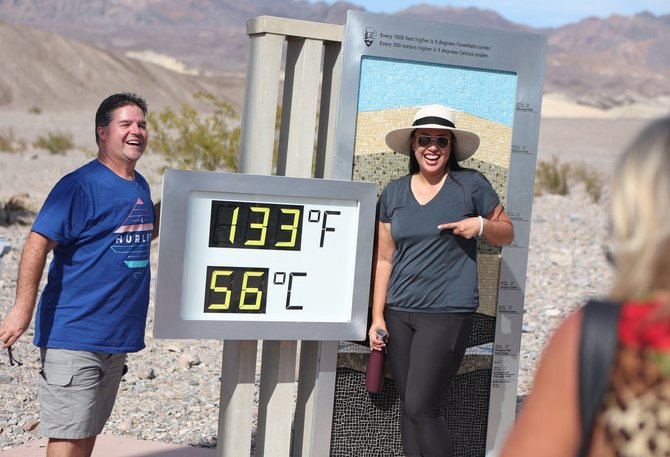 AFP/„Scanpix“ nuotr./Turistai Mirties slėnyje darosi asmenukę prie rekodrinę temperatūrą rodančio termometro