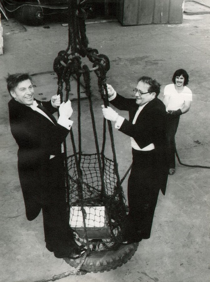 LTMKM nuosavybė/Organizacijos „Lenkoncert“ muzikantai – dainininkas J. Jocys ir pianistas G. Basas. Artistus kranu kelia į laivą, kur vyks koncertas žvejams. ~1978 m. Nuotr. aut. nežinomas.