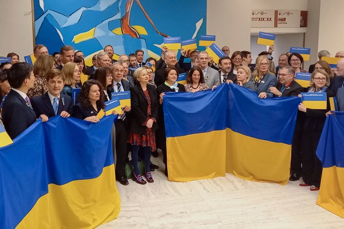 „AFP“/„Scanpix“/Ambasadoriai ir atstovai su Ukrainos vėliavomis ir plakatais "StandWithUkraine" pozuoja nuotraukai prie Jungtinių Tautų Nusiginklavimo konferencijos salės, Rusijos užsienio reikalų ministro pavaduotojui sakant kalbą