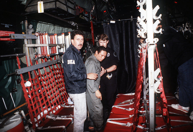 Wikipedia.org nuotr./JAV Narkotikų kontrolės administracijos pareigūnų lydimas Manuelis Noriega lėktuve, skrisiančiame į JAV (1990 m. sausio 3 d.)