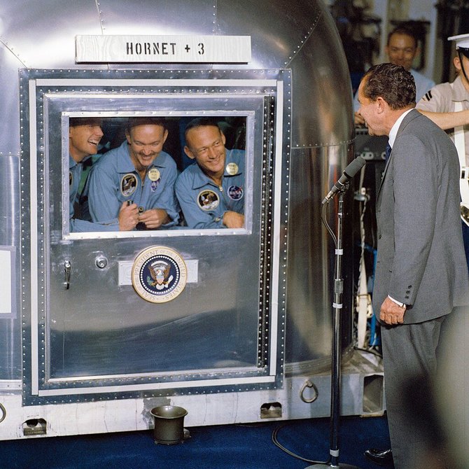 NASA nuotr./Richardas Nixonas su „Apollo 11“ astronautais, kurie po sugrįžimo iš Mėnulio lėktuvnešyje „Hornet“ uždaryti į karantino kapsulę. 1969 m. liepos 24 d.