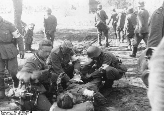 Vokietijos bundesarchyvo/Wikimedia.org nuotr./Pirmoji karo diena. Vokiečių karo medikai suteikia pagalbą sužeistam kariui.
