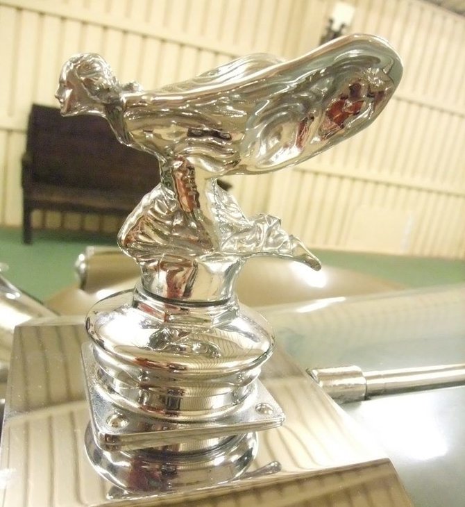 Rolls-Royce 1934–1939 ir 1946–1956 metais buvo puošiamas klūpinčia skulptūrėlės versija, kad sportiškų automobilių vairuotojai geriau matytų kelią. (Javi Guerra Hernando, Wikimedia(CC BY-SA 4.0)