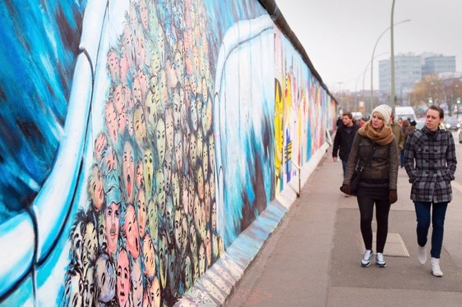 123rf.com nuotr./Žmonės einantys pro Berlyno sienos rytų pusės galeriją. Ji yra 1.3km ilgio dalis originalios sienos, kuri sugriuvo 1989 metais ir dabar tai didžiausia grafiti galerija pasaulyje