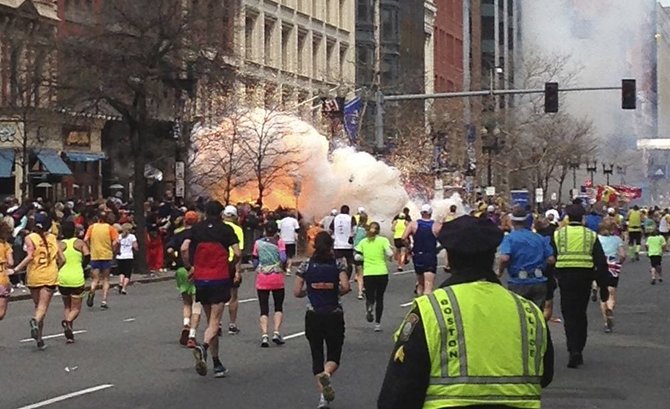 Bostono maratono dalyviai bėga link finišo, kairėje pusėje matomas prasidėjęs sprogimas.