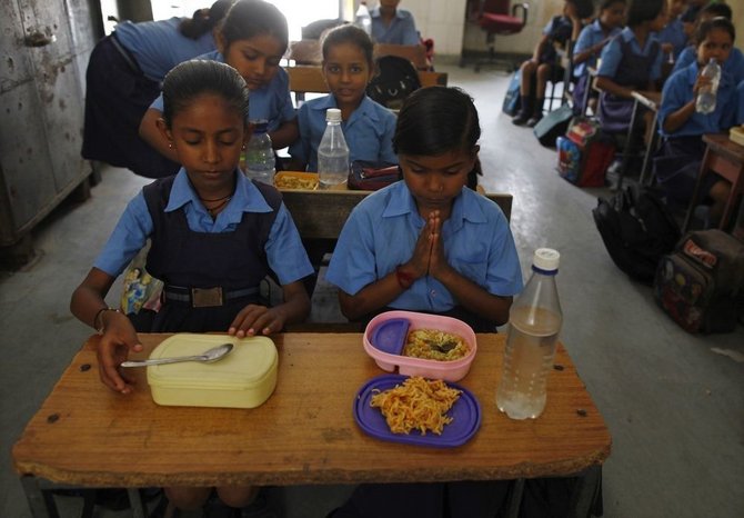 „Reuters“/„Scanpix“ nuotr./Indijos mokykloje mokiniai meldžiasi prieš valgydami pietus. 