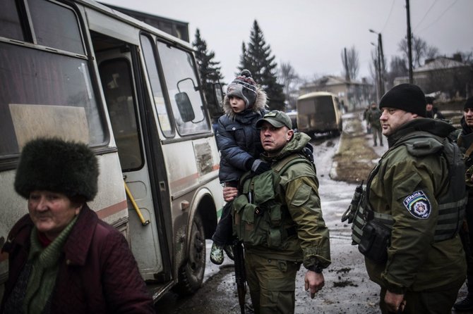 AFP/„Scanpix“ nuotr./Ukrainos karys neša vaiką į autobusą, kuriuo evakuojami žmonės iš Debalcevės miesto.