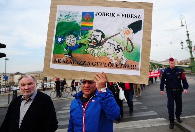 „Reuters“/„Scanpix“ nuotr./Protestuotojas laiko plakatą, kuriame lygina valdančiąją Fisesz partiją su ultradešiniaisiais Jobbik