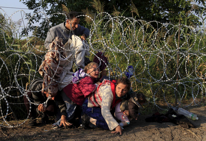 „Reuters“/„Scanpix“ nuotr./Vengrija, 2015 rugpjūčio 27 d. Migrantų šeima iš Sirijos bando pralįsti pro spygliuotą vielą prie sienos su Serbija