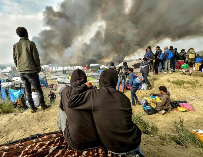 AFP/„Scanpix“ nuotr./Migrantai stebi gaisrą Kalė stovykloje