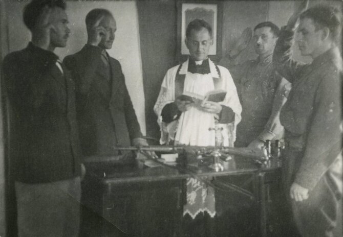 Genocidų aukų muziejaus fondų nuotrauka/Pirmojo Tauro apygardos štabo pareigūnų priesaika 1945 m. liepos 19 d. Viduryje – vienas apygardos kūrėjų kapelionas Antanas Ylius–Vilkas. Iš kairės – Jonas Pileckis–Brokas, Leonas Taunys–Kovas, Albinas Ratkelis–Oželis, Vytautas Gavėnas–Vampyras. 