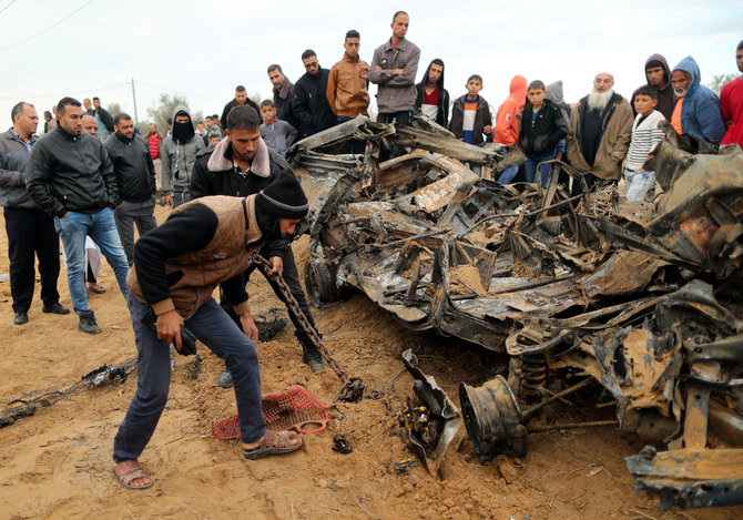 „Reuters“/„Scanpix“ nuotr./Palestiniečiai prie automobilio, sunaikinto per aviacijos smūgio, nuolaužų