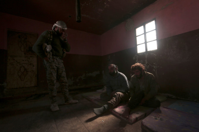 „Reuters“/„Scanpix“ nuotr./SDF karys prie į nelaisvę paimtų IS kovotojų